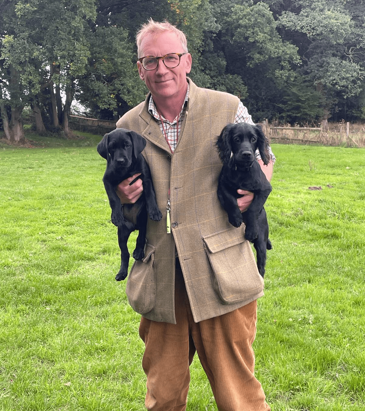 Man holding two black puppies in field